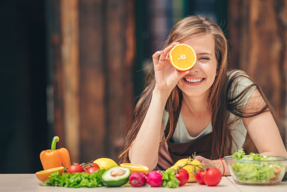 Ragazza sorridente davanti a un tavolo di frutta e verdura, cibi ottimi per la salute oculare